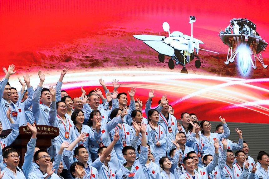 A crowd of people at the Beijing Aerospace Center throw their hands in the air and shout after a Mars landing.