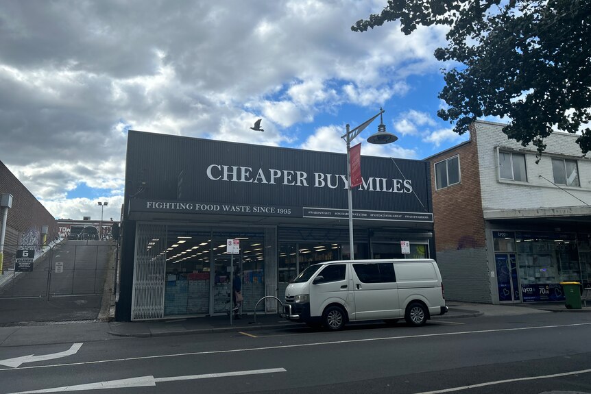 A photograph showing the outside of discount store, Cheaper Buy Miles, which is a black store with white font out front.