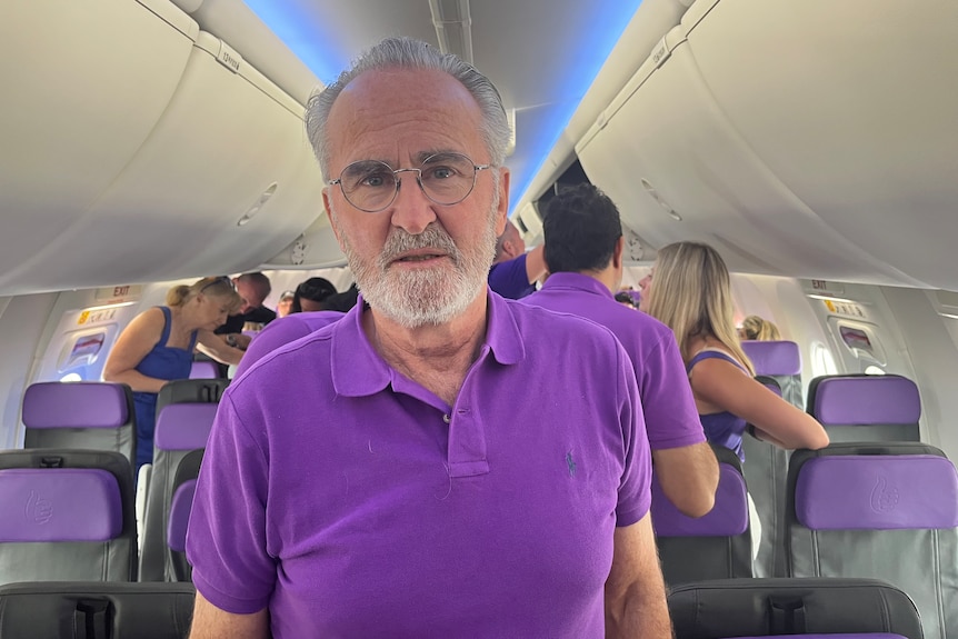 caucasian man with beard and glasses wearing a purple shirt standing on a plane