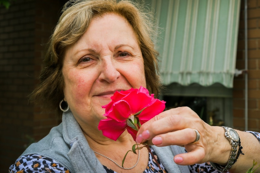 A woman pulls a rose towards her face so she can smell the flower