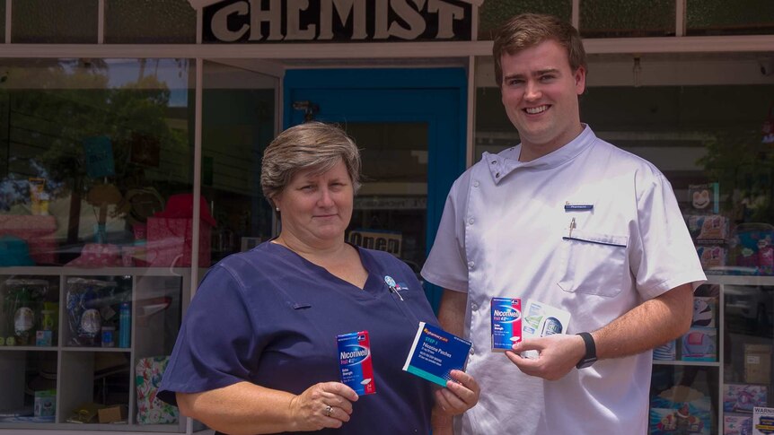 A woman in a nurses' uniform and man in pharmacist's white shirt standing outside an old shop front with the word chemist on it
