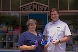 A woman in a nurses' uniform and man in pharmacist's white shirt standing outside an old shop front with the word chemist on it