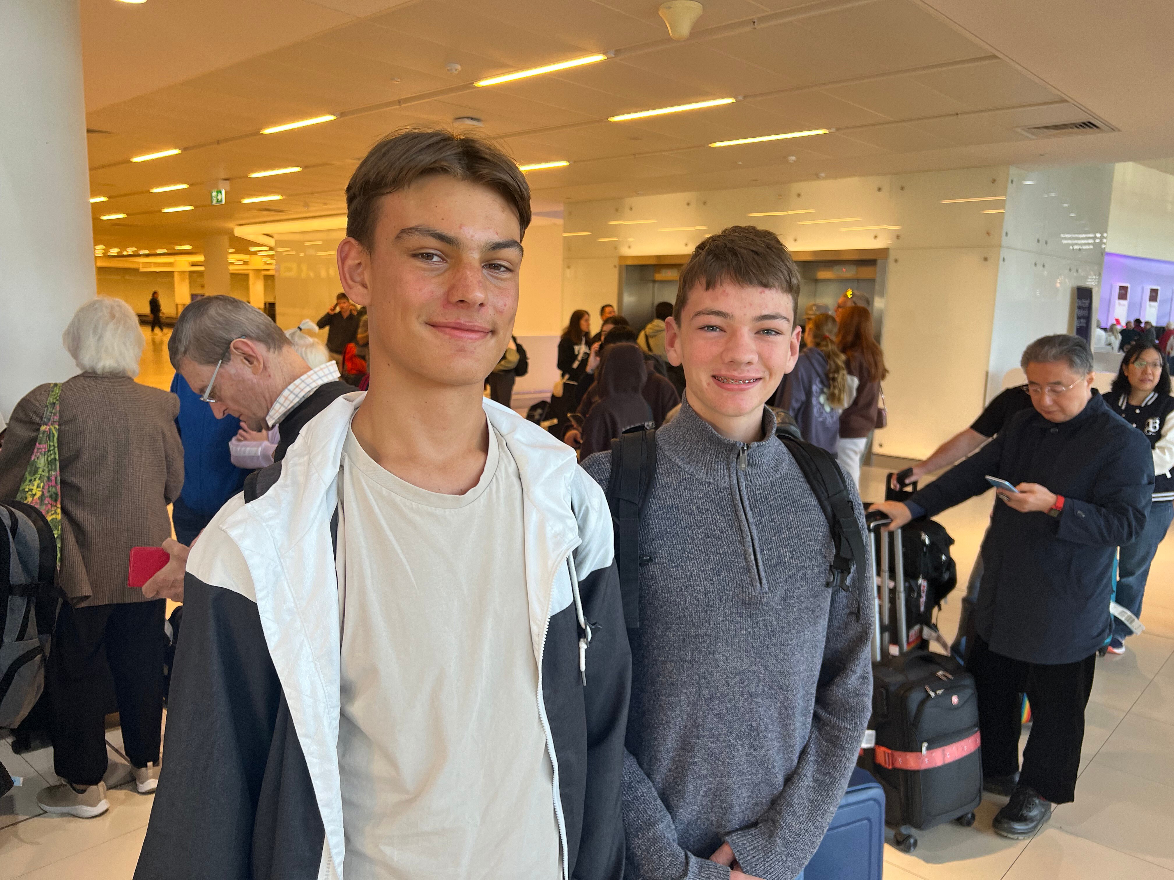 Two young men in a busy airport terminal smile at the camera.