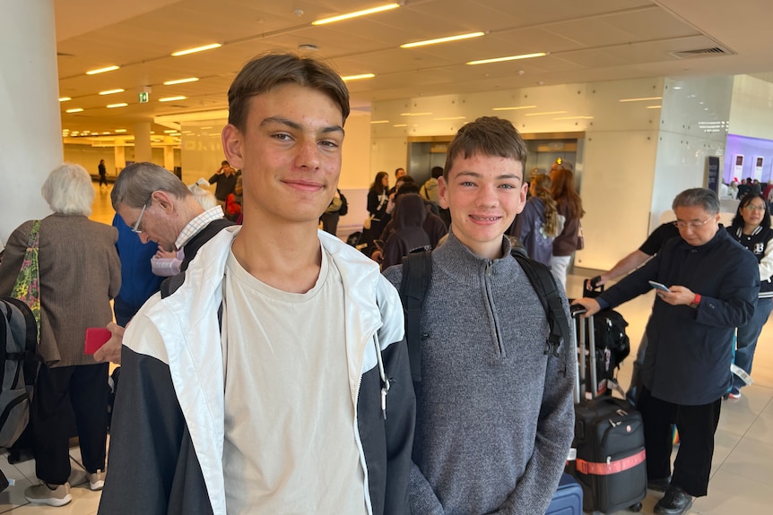 两个年轻人在拥挤的机场休息室里对着镜头微笑。