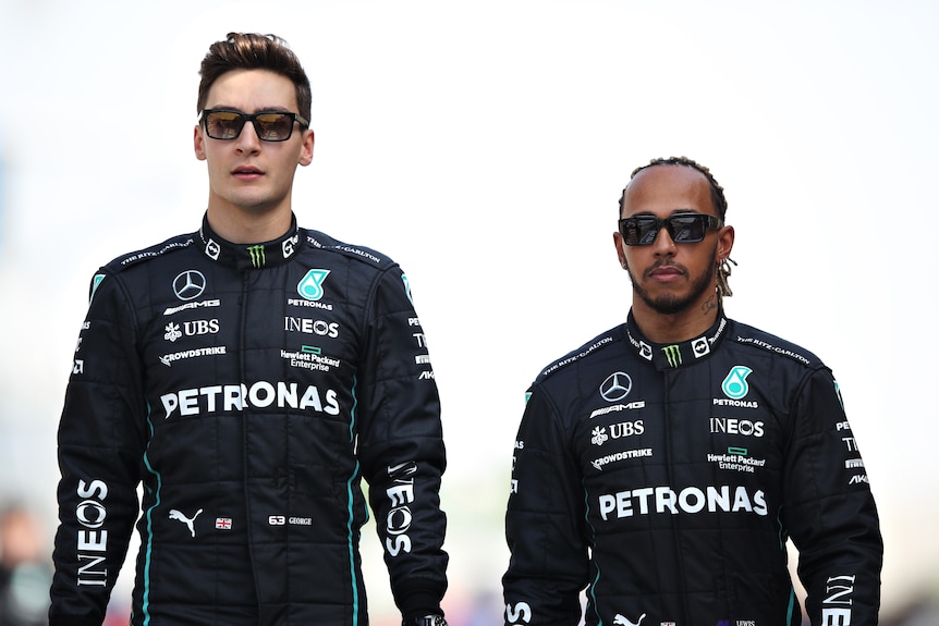 Two F1 teammates, out of the car, wearing sunglasses, walking down the track.