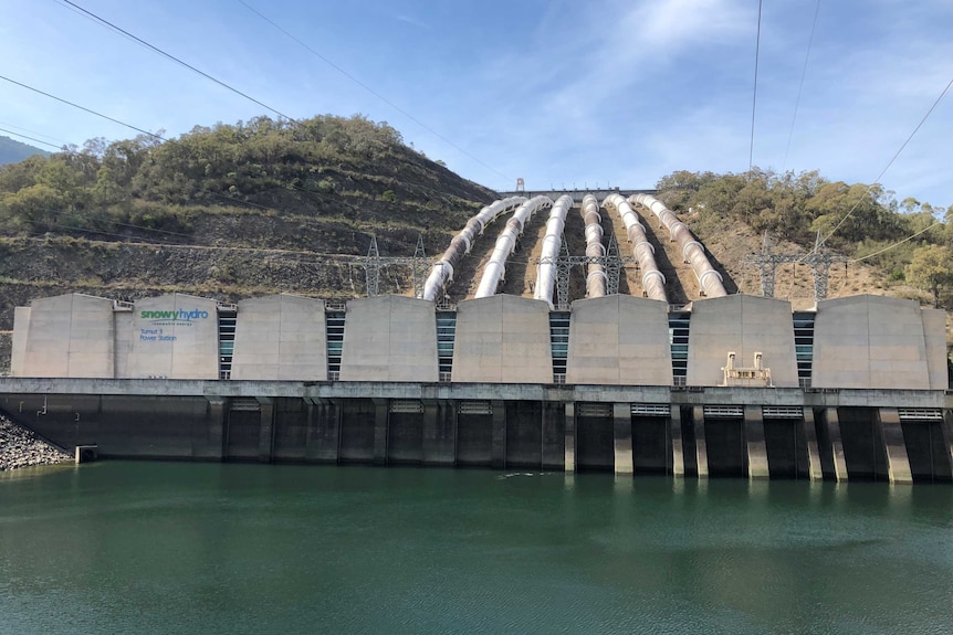 Six pipelines come over the crest of the hill and into the power station building, which sits over a small lake.