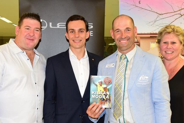 Three men and one woman standing next to each other smiling at the camera with one man holding a book