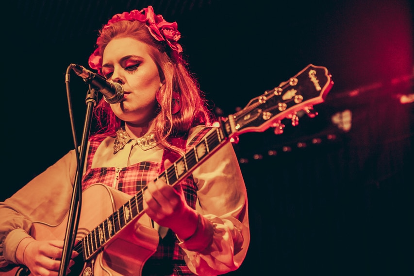 Women stands on stage playing guitar