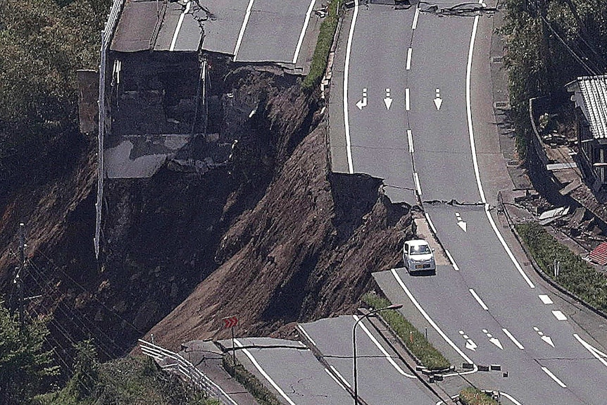 Elevated view of a car sitting half on, half off the edge of a collapsed road on the side of a mountain.