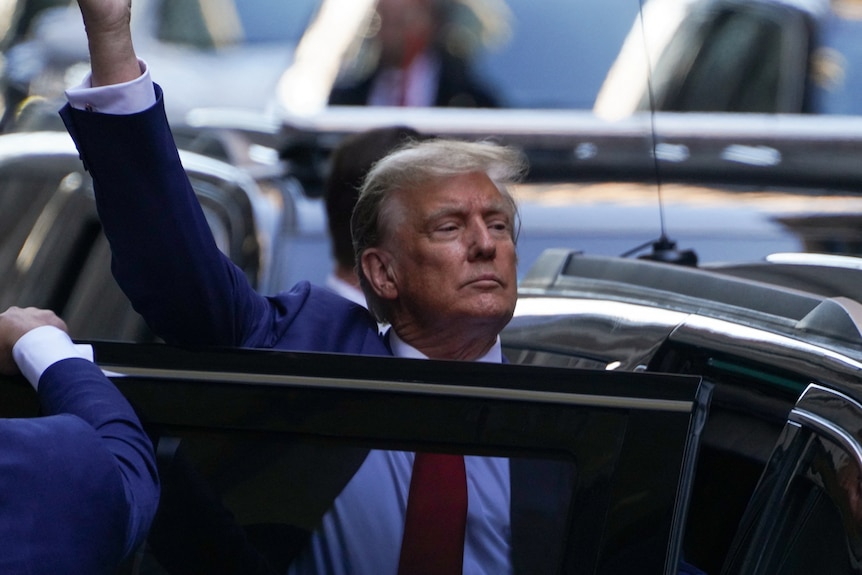 Donald Trump raises a hand as he steps into a car 