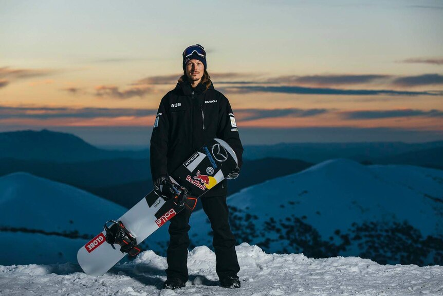 Winter Olympian and Australian snowboarder Alex 'Chumpy' Pullin stands with his snowboard on a snow-covered mountain.