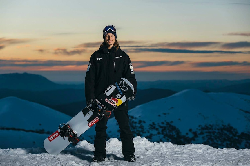 Winter Olympian and Australian snowboarder Alex 'Chumpy' Pullin stands with his snowboard on a snow-covered mountain.