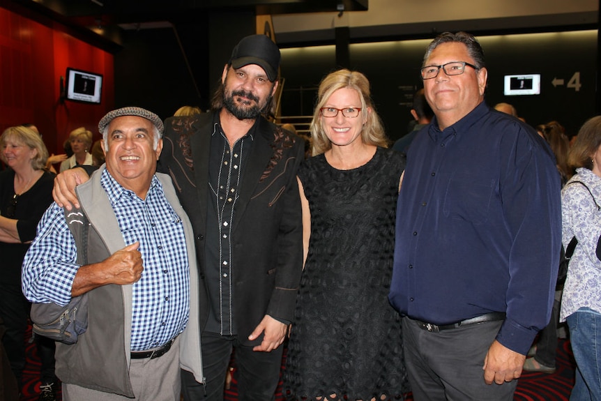 Four people standing side by side in a theatre.