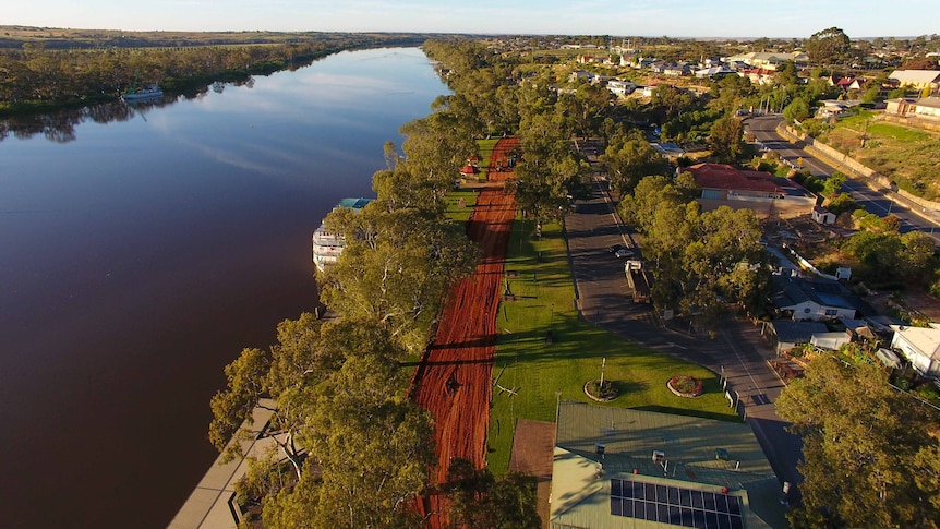 An aerial shot of a town with the wide river to the left, levee in the middle and town to the right.