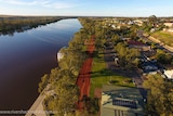 An aerial shot of a town with the wide river to the left, levee in the middle and town to the right.