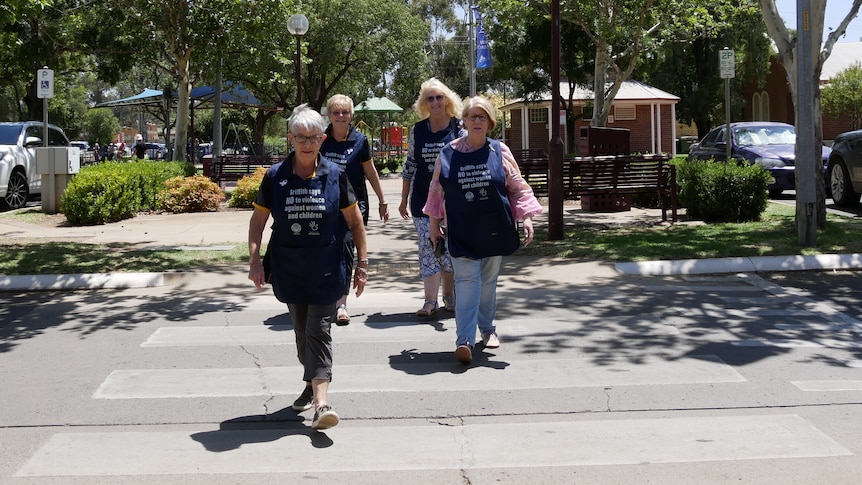 Four women in matching aprons crossing a street.