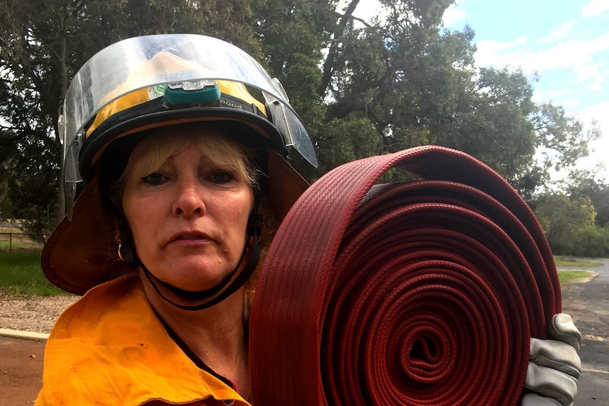 Woman in firefighting uniform holds a rolled up large red hose