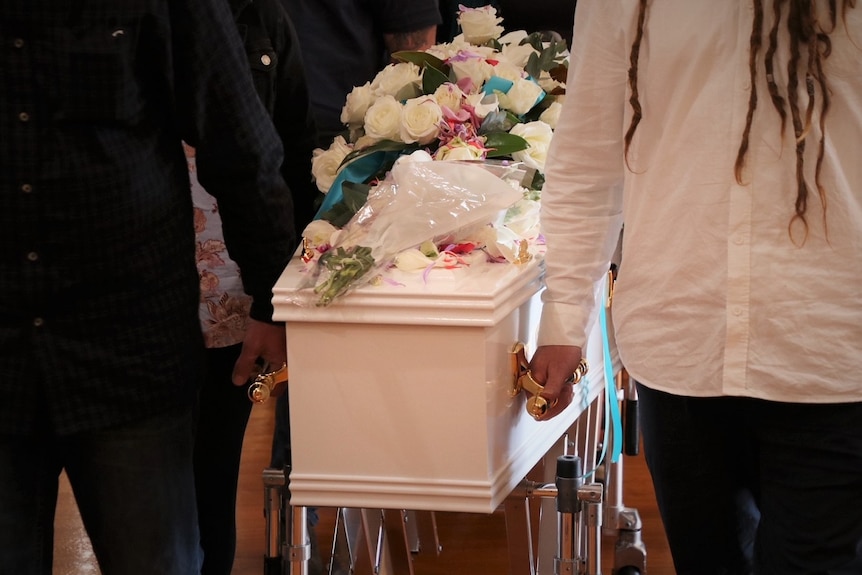 Funeral casket carried by mourners on trolley.