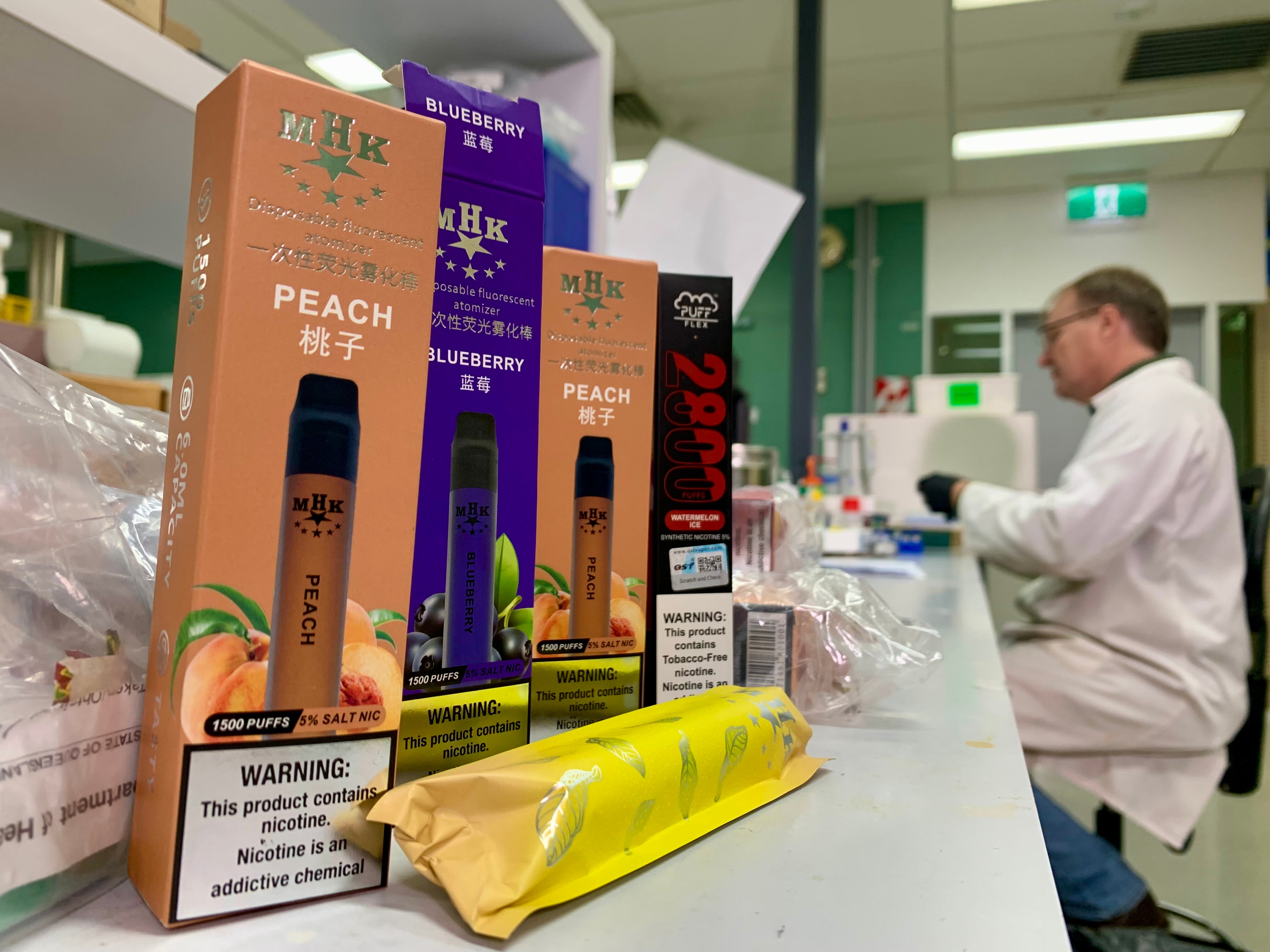 David Pass sits in the in Queensland Health's Forensic and Scientific Services lab, boxes of vapes stand nearby
