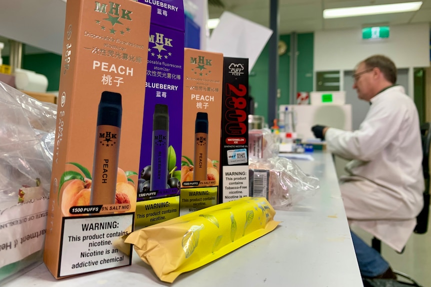 David Pass sits in the in Queensland Health's Forensic and Scientific Services lab, boxes of vapes stand nearby