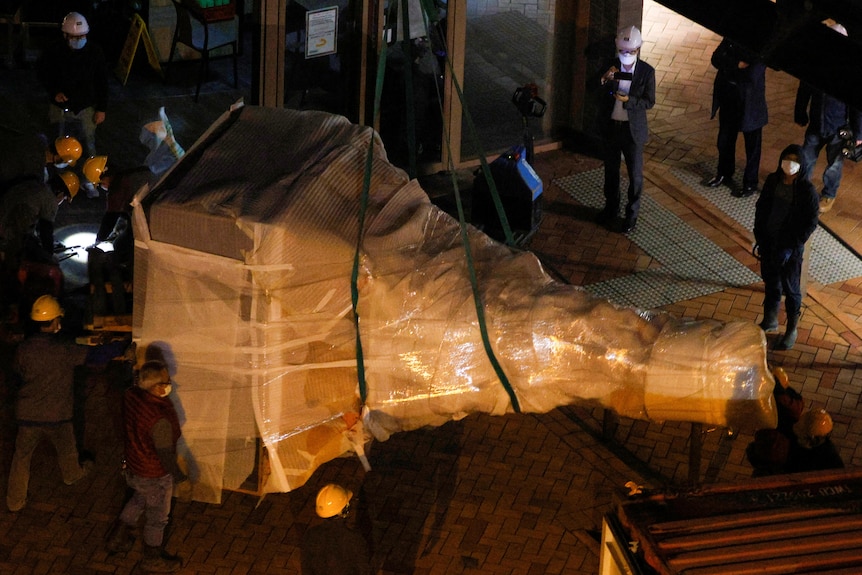 Workers remove a part of the "Pillar of Shame" sculpture.