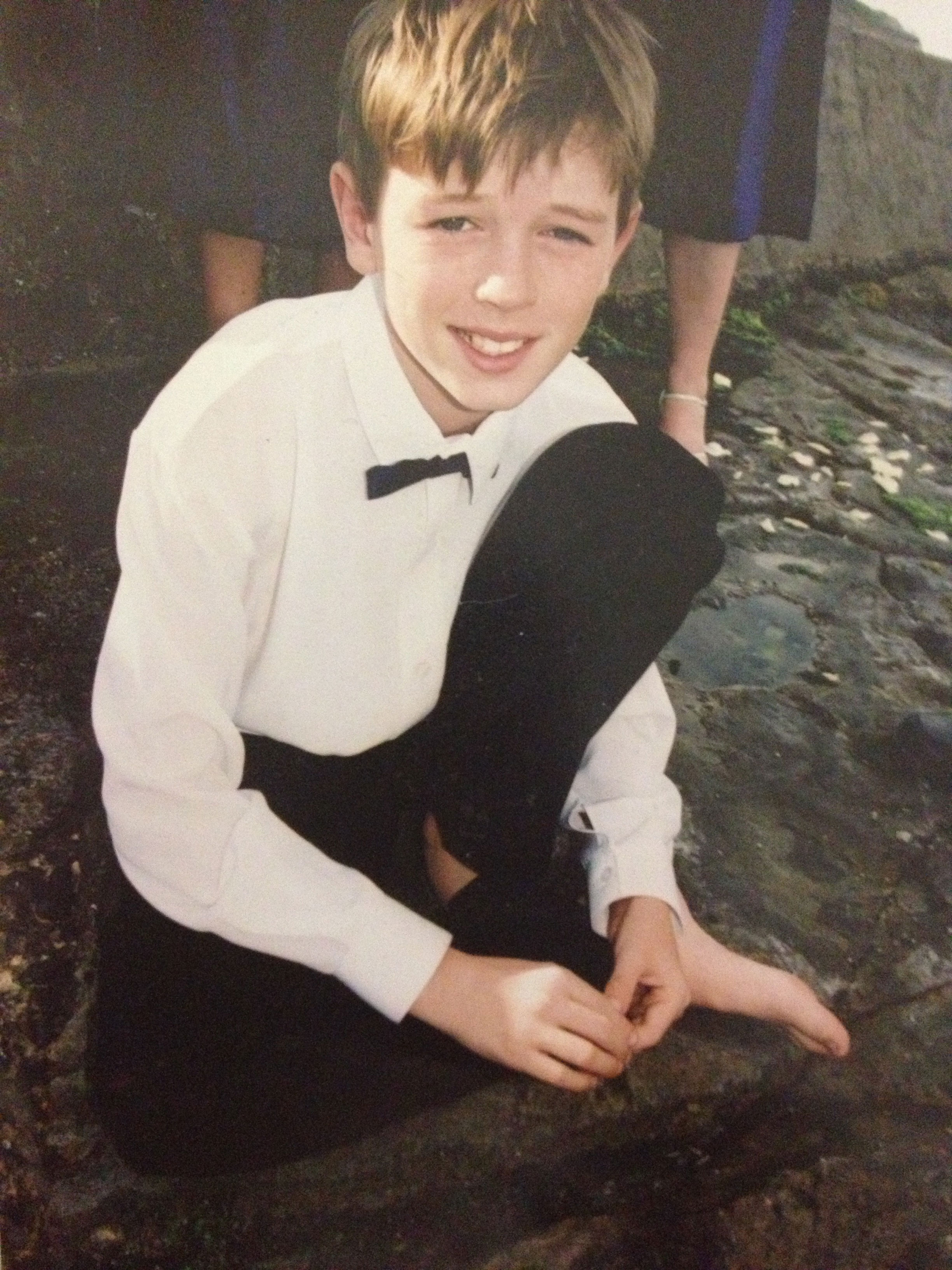 Boy wearing white shirt, black tie and pants, crouching on ground.