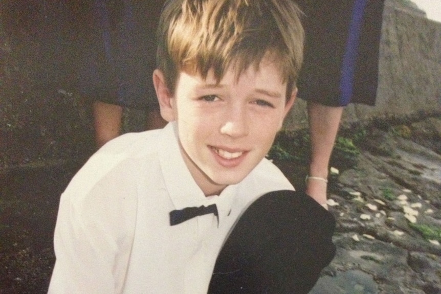 Boy wearing white shirt, black tie and pants, crouching on ground.