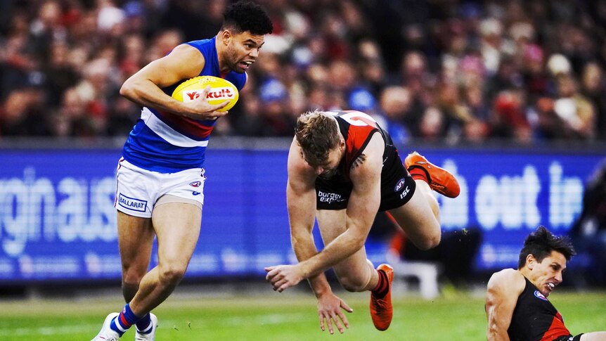 Carrying the ball, Jason Johannisen runs away from Jake Stringer who is airborne after a failed tackling attempt.