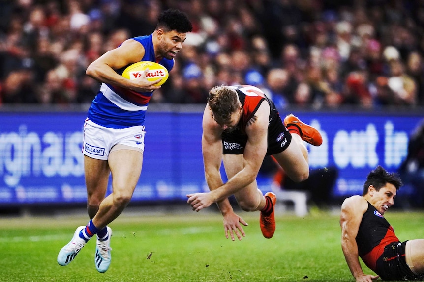 Carrying the ball, Jason Johannisen runs away from Jake Stringer who is airborne after a failed tackling attempt.