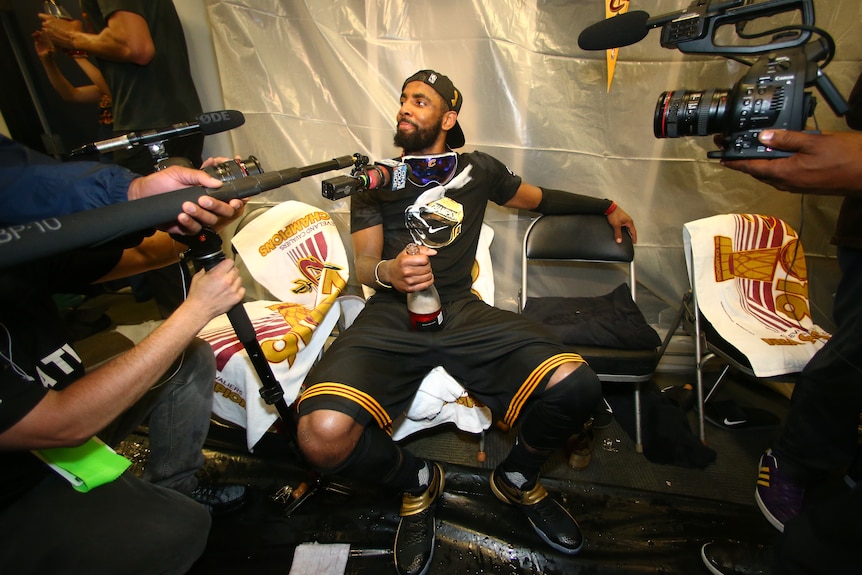 Media aims cameras and microphones at Cleveland's Kyrie Irving as he sits with a champagne bottle after winning the NBA Finals.