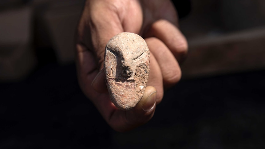 A hand holds a small, old rock, seemingly carved into the shape of a face.