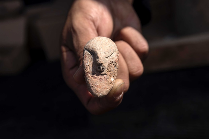 A hand holds a small, old rock, seemingly carved into the shape of a face.