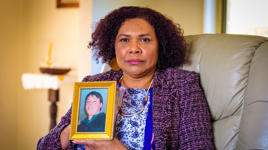 A woman holds a framed photo of a man.