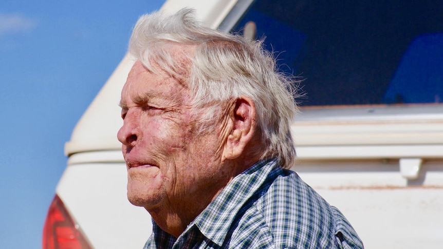 an older man looking away from the camera with a ute behind.