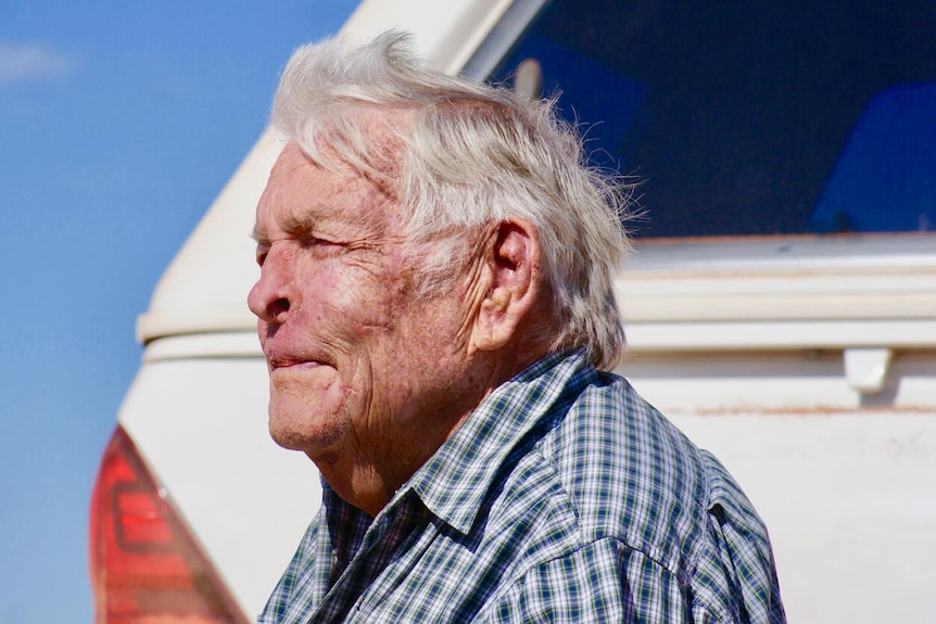 an older man looking away from the camera with a ute behind.