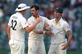 Pat Cummins, Mitchell Starc and Cameron Green hug with neutral expressions on their faces