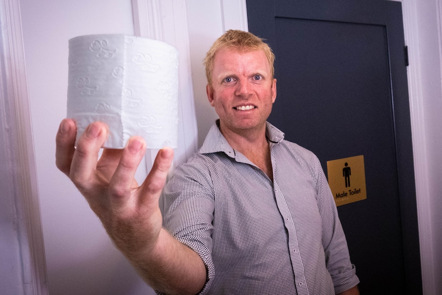 A man holds a toilet roll next to a men's toilet