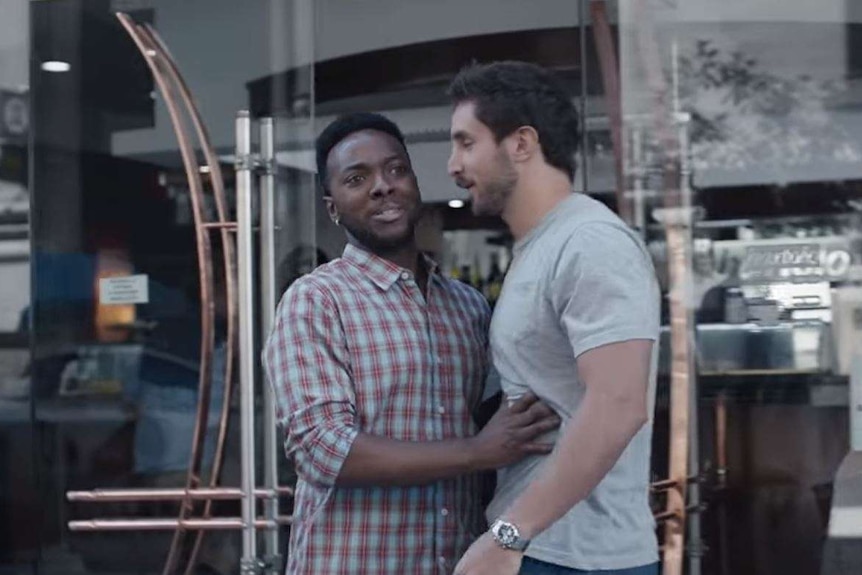 A man holds another man from walking down a city street.