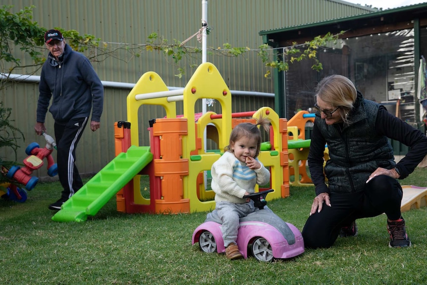 Barb in her day care playing with a young girl, while Rocky walks by in the background.