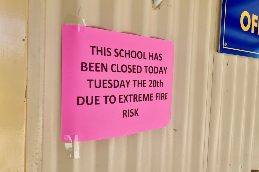   Un cartel rosa en una pared que advierte del cierre de una escuela debido al riesgo extremo de incendio.