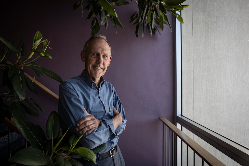Bob Brown stands next to a large rubber plant growing inside a building stairwell.