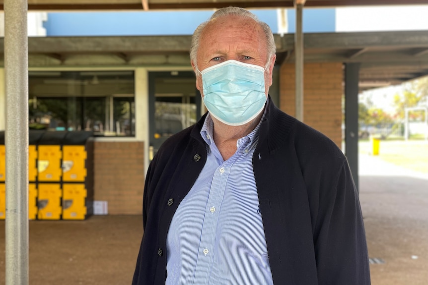 A man in a surgical mask standing in front of a school