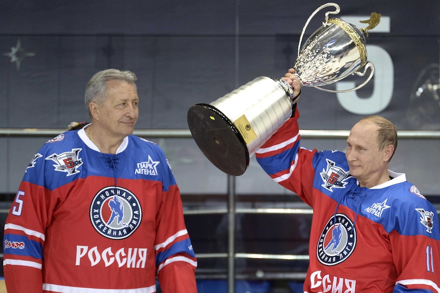 Former ice hockey player Alexander Yakushev watches Russian President Vladimir Putin lift a trophy after a gala ice hockey game.