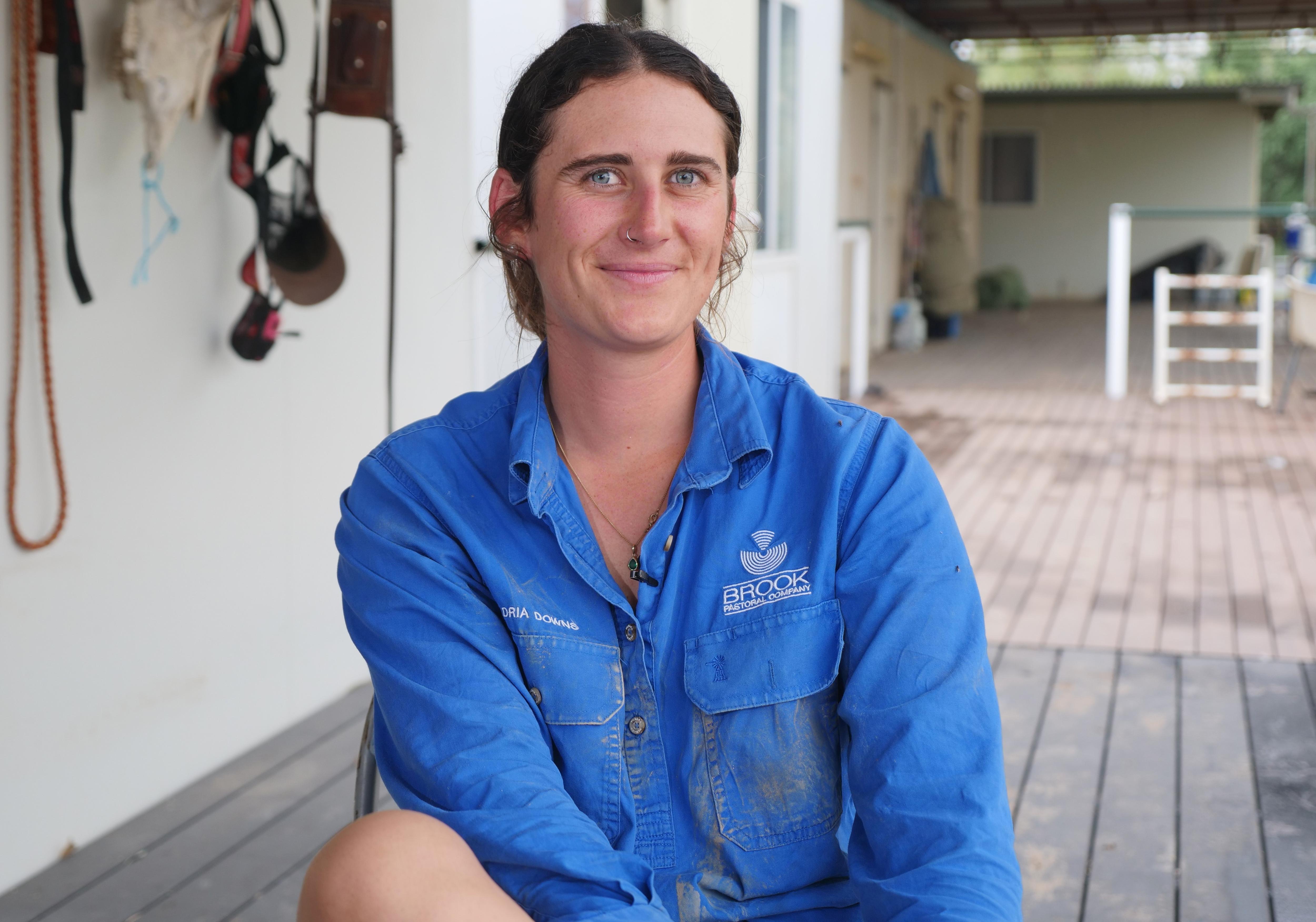 Storm Foxwell com uma camisa de trabalho azul sentada no terraço da sala dos funcionários sorrindo para a câmera.