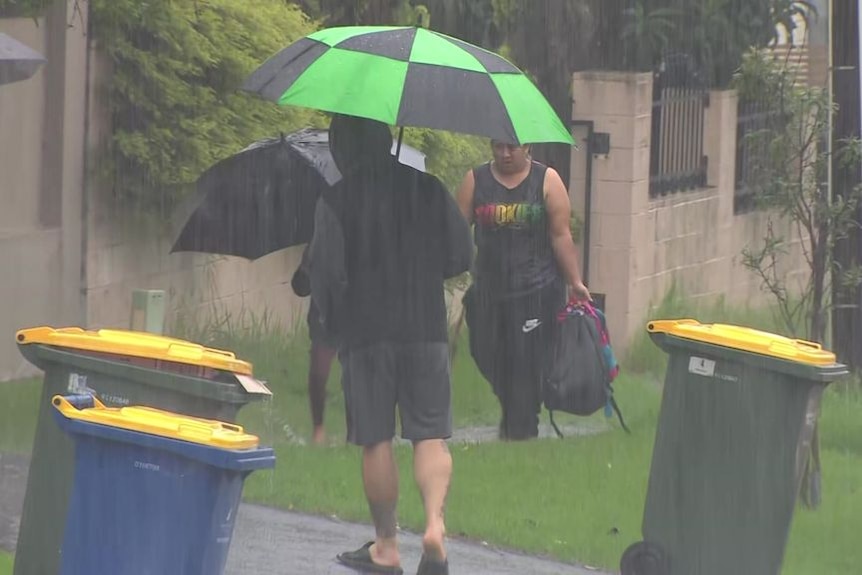 People holding umbrellas walk through rain.