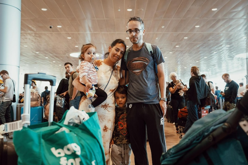 A woman, a man and two young children look at the camera, surrounded by luggage and other people