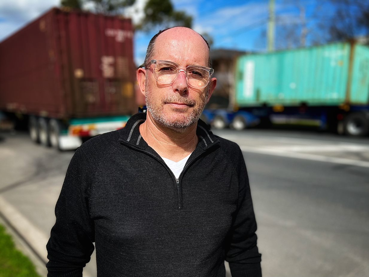 Martin Wurt, wearing clear-rimmed glasses and a black top, stands in front of container trucks.