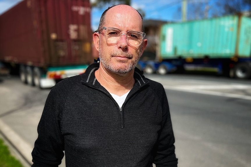 Martin Wurt, wearing clear-rimmed glasses and a black top, stands in front of container trucks.