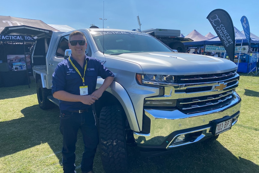 Young man in a blue button up shirt stands next to a four wheel drive truck