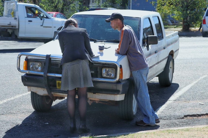 A woman and a man speak near a large car.